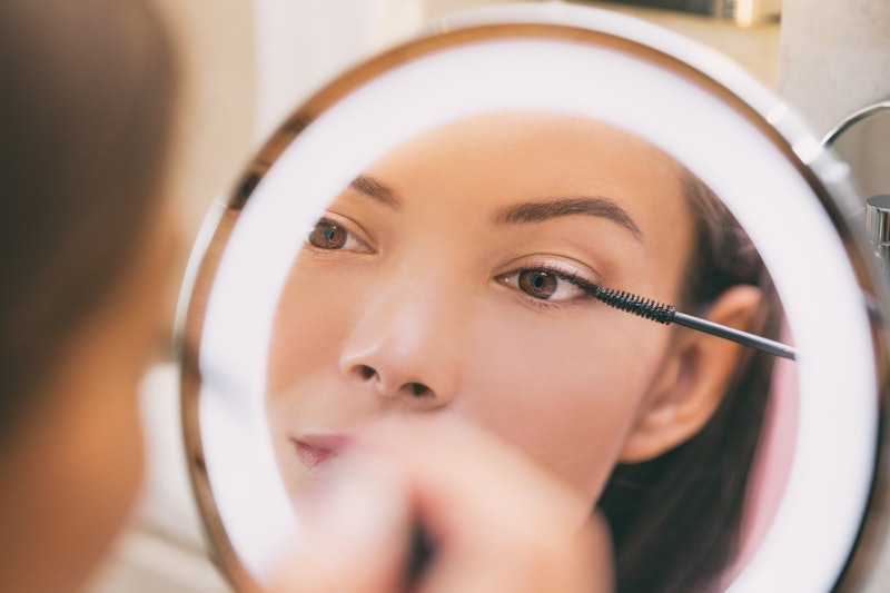 woman applying mascara in front of a mirror — starting with a waterproof formula is a way to avoid m...
