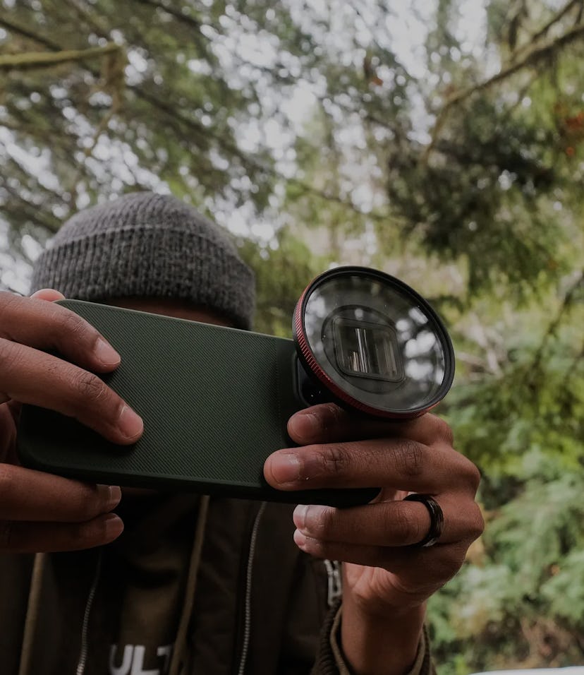 A man holding a smartphone with an attached add-on lens.
