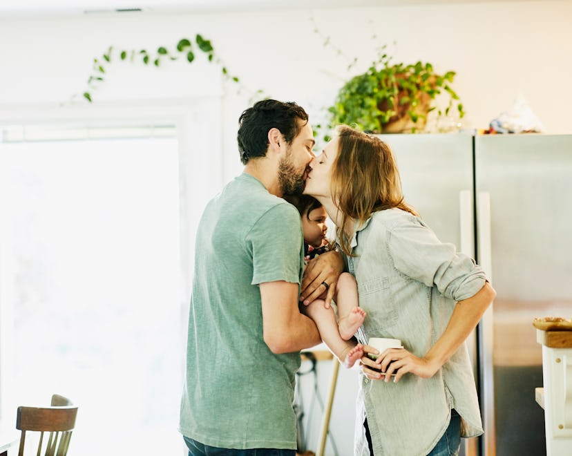couple sweetly kissing in kitchen, holding infant between them, love captions for instagram