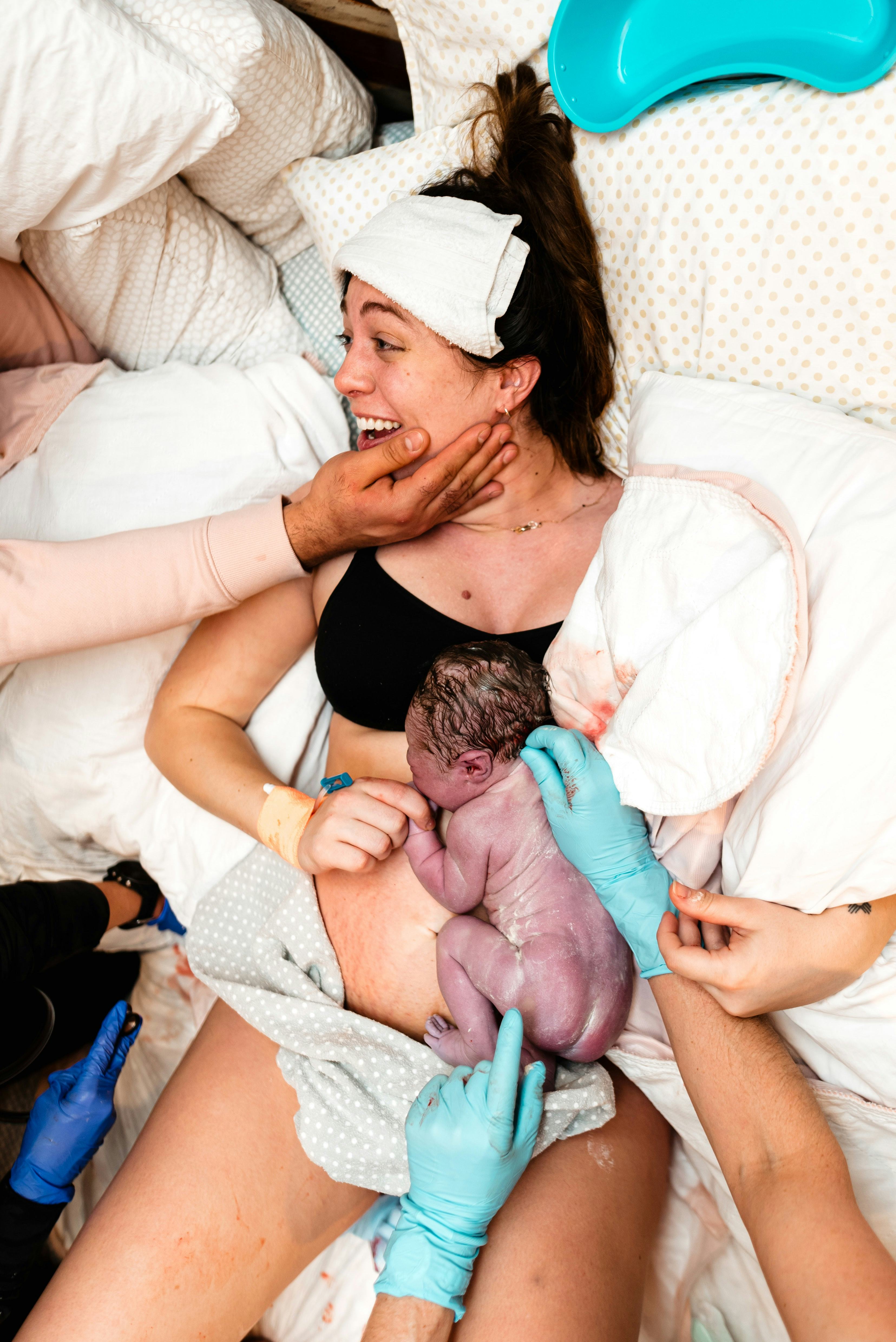 a woman smiles while holding her newborn after birth