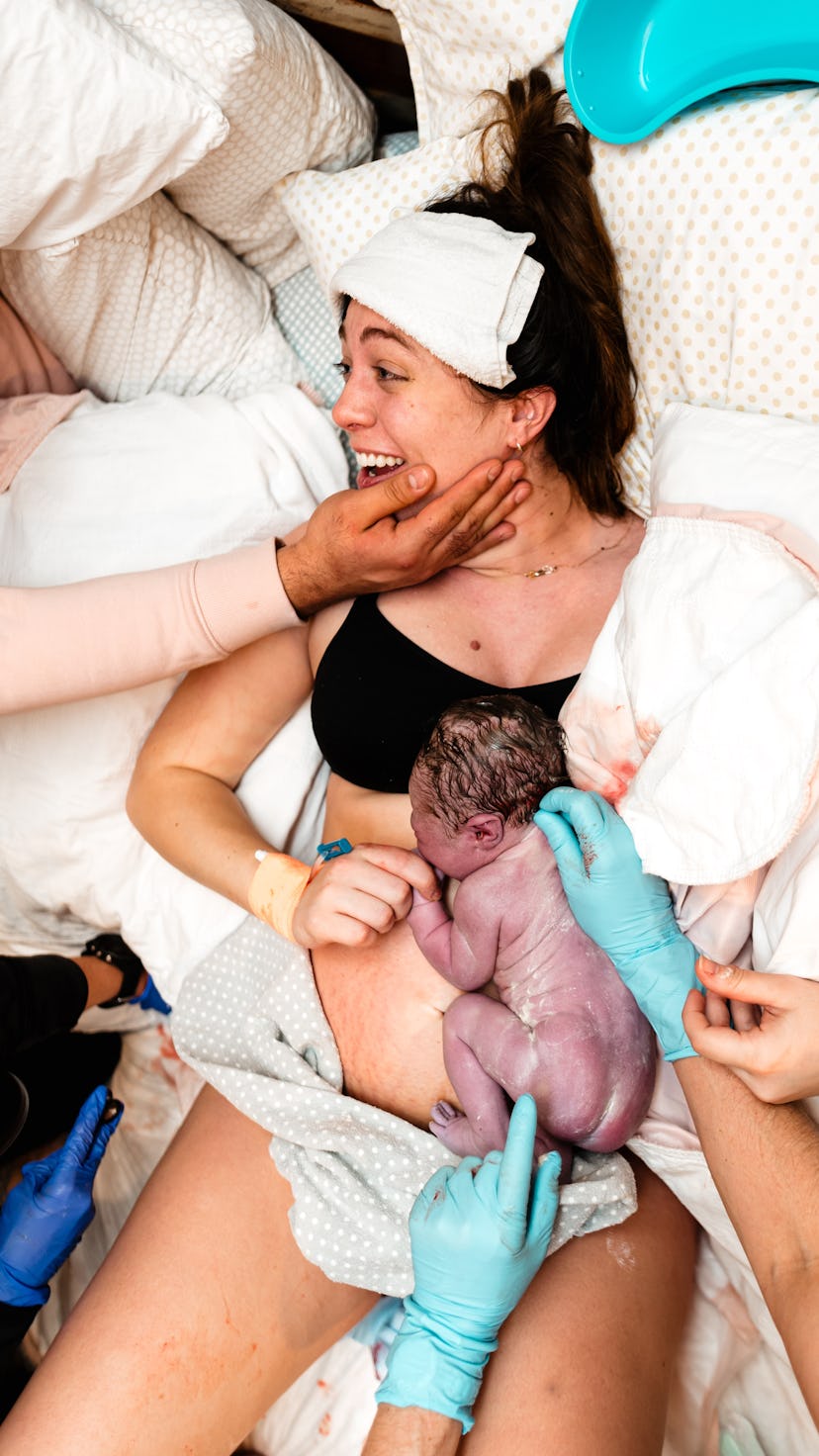 a woman smiles while holding her newborn after birth
