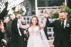 A bride in a white dress and a groom walking down the aisle and smiling on their wedding in the midd...