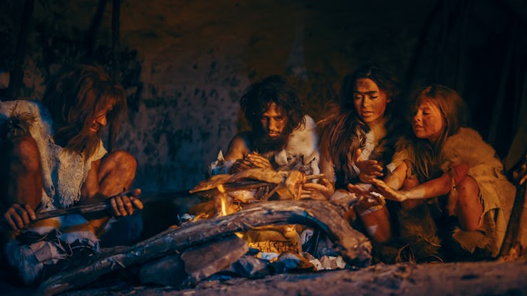 Tribe of Prehistoric Hunter-Gatherers Wearing Animal Skins Grilling and Eating Meat in Cave at Night