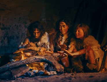 Tribe of Prehistoric Hunter-Gatherers Wearing Animal Skins Grilling and Eating Meat in Cave at Night