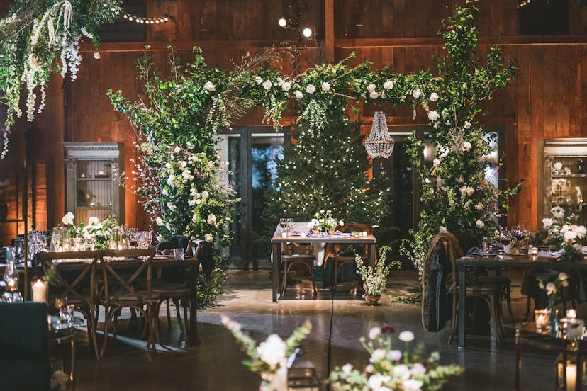 The inside of the wedding venue with tables for the guests and various green plant deco placed on th...