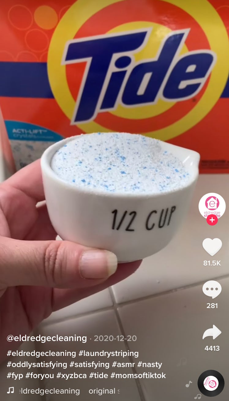 A woman holds some laundry detergent in front of a Tide box in her bathroom. 