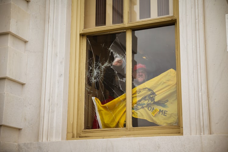 A member of a pro-Trump mob shatters a window with his fist from inside the Capitol Building after b...