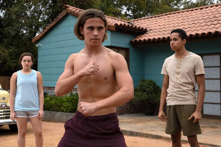 Shirtless Robbie standing in a fighting stance next to two kids in front of a blue house