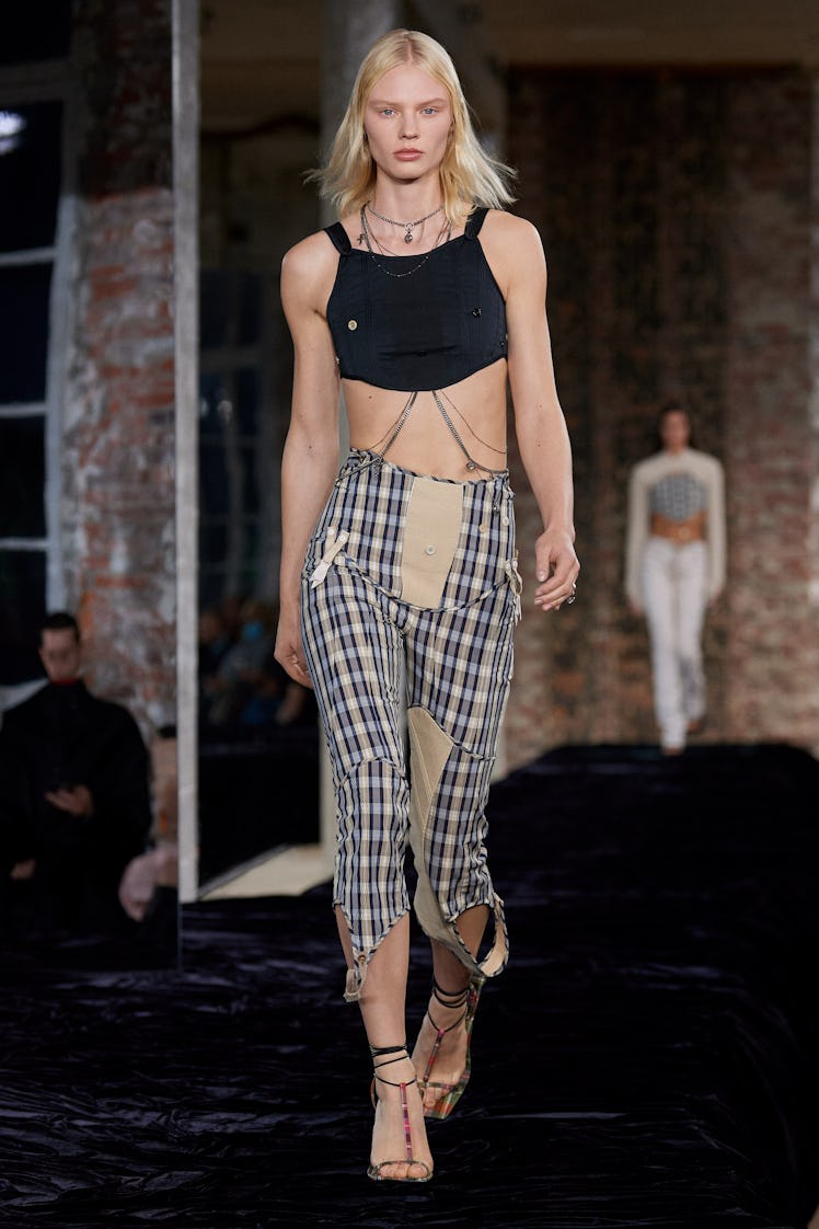 A model walking in a black top and grey check pants by Acne Studios