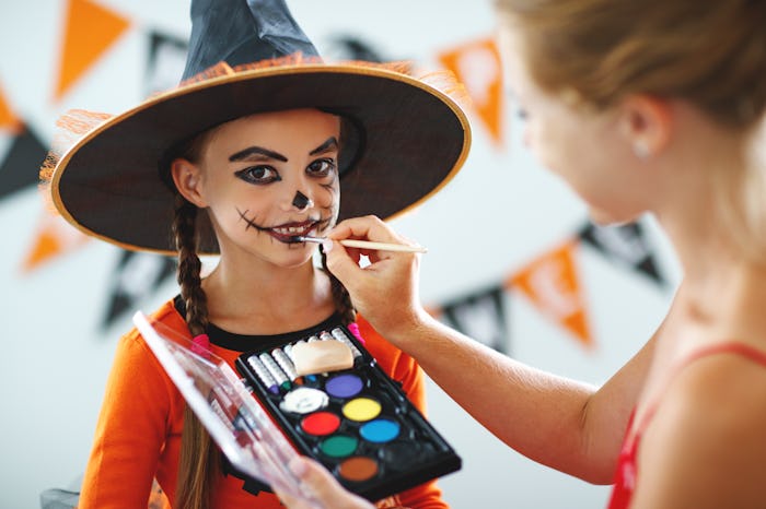 A young woman painting a face of a girl dressed in a witch costume