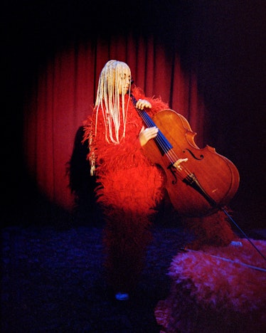 A woman playing the cello in a red feather Bottega Veneta outfit 