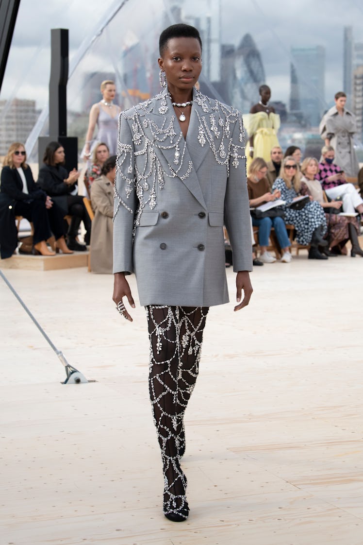Model walking in a grey coat with silver beads at the Alexander McQueen Spring 2022 show.