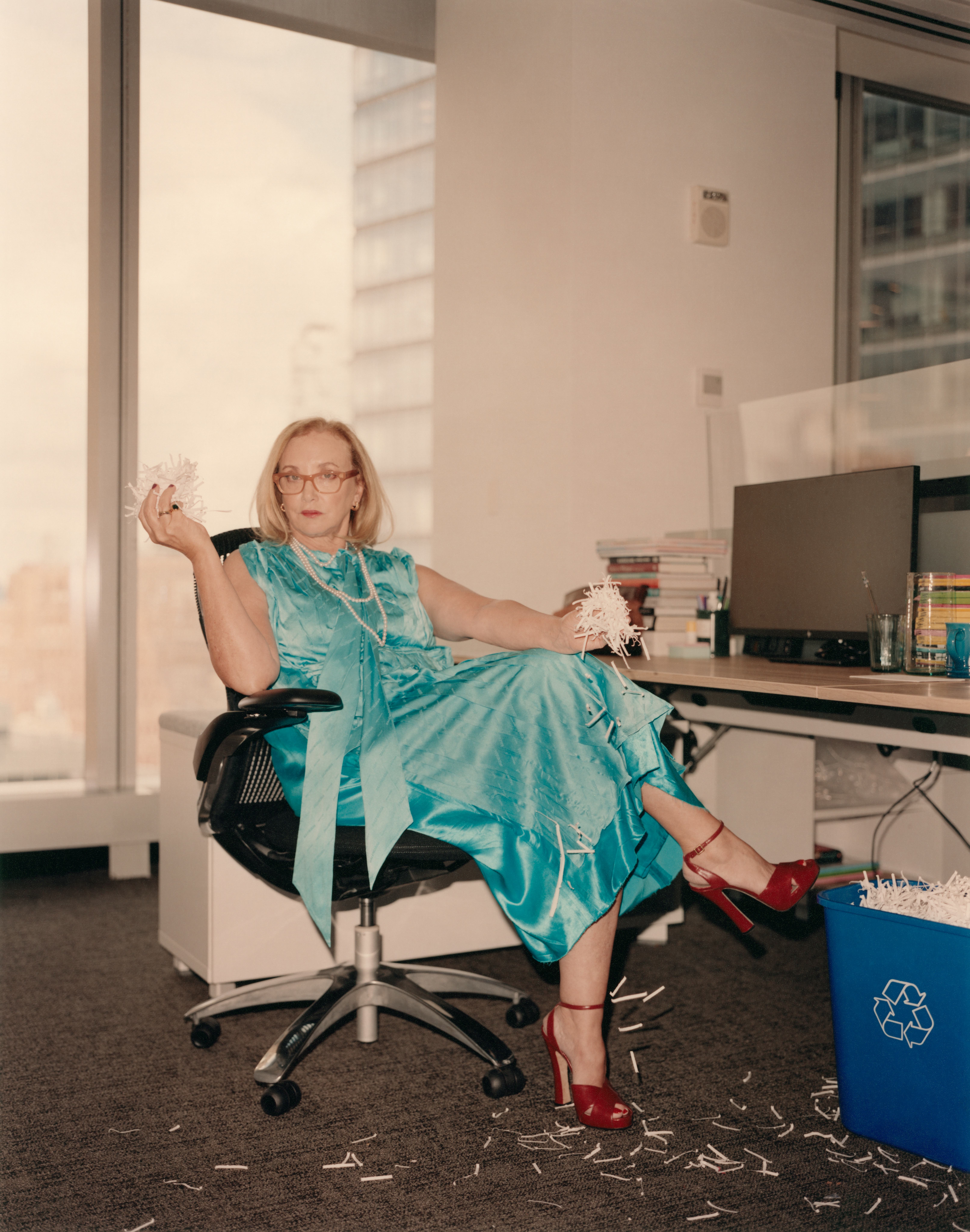 J. Smith-Cameron in an office sitting on a chair in a blue satin dress