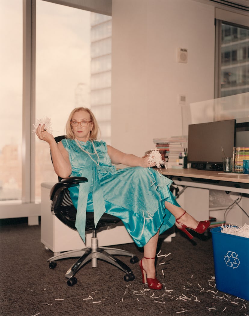 J. Smith-Cameron in an office sitting on a chair in a blue satin dress