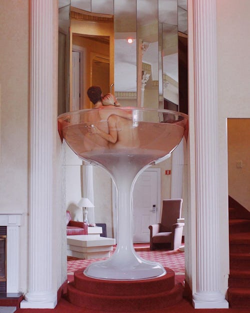 Margaret and Corey Bienert laying naked in an enlarged martini glass at a hotel
