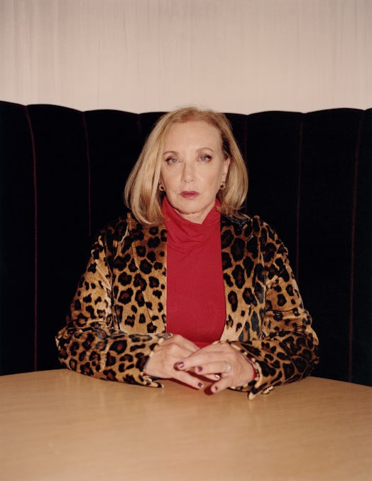 J. Smith-Cameron in a red turtleneck and a leopard-print coat sitting and posing