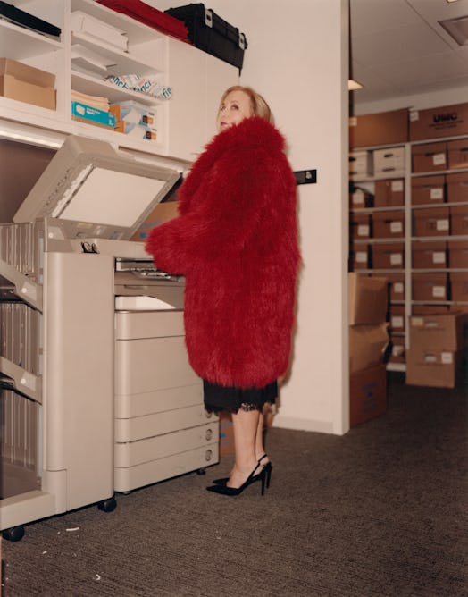 J Smith-Cameron in red coat standing next to a copy machine.