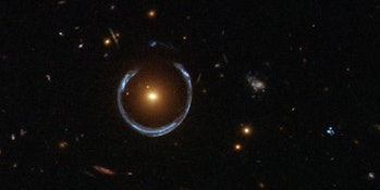 An image of a blue galaxy as viewed through the gravitational lensing effect from a bright red galax...