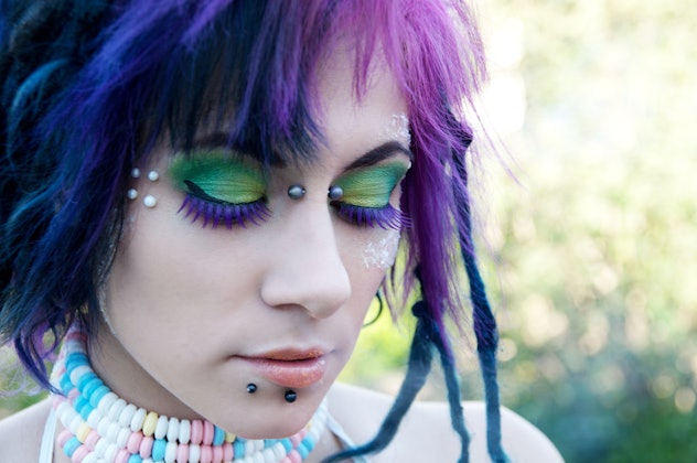 Woman looking down, with green eye shadow, purple false lashes, and gems