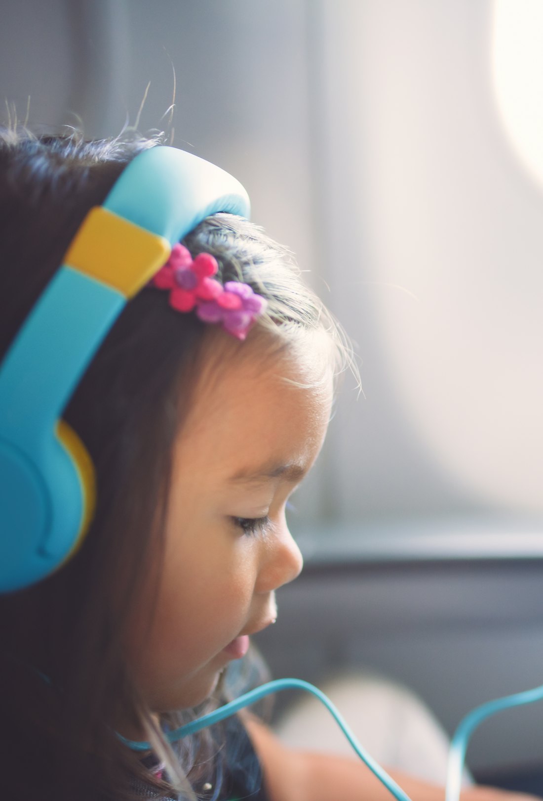young girl on airplane, listening on headphones and watching her tablet 