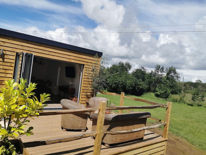 A wooden lodge in Dorset's Purbeck countryside with a secluded deck with two armchairs, a patio couc...