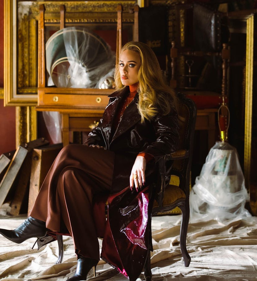 Adele in “Easy on Me” video, siting in a long black coat and brown trousers