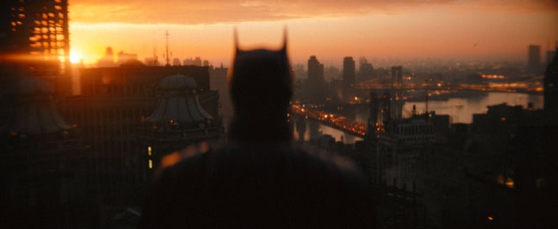 A blurred Batman looking at the skyline of a city during a sunset
