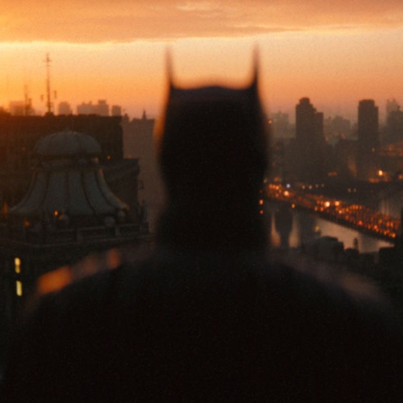 A blurred Batman looking at the skyline of a city during a sunset