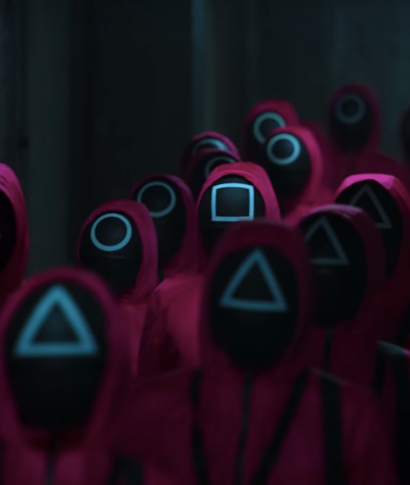 A group of people wearing pink hooded jumpsuits with their faces covered by black masks adorned with...