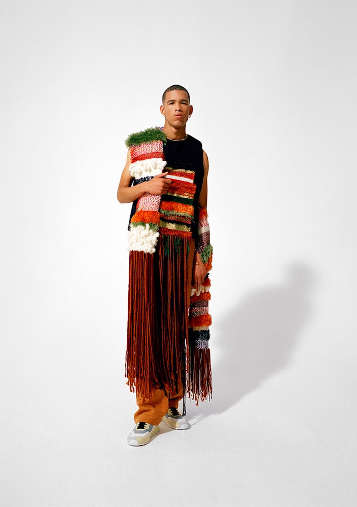 A model wearing a black top with a knit stripe and a long fringe, and a multi-colored knit scarf by ...