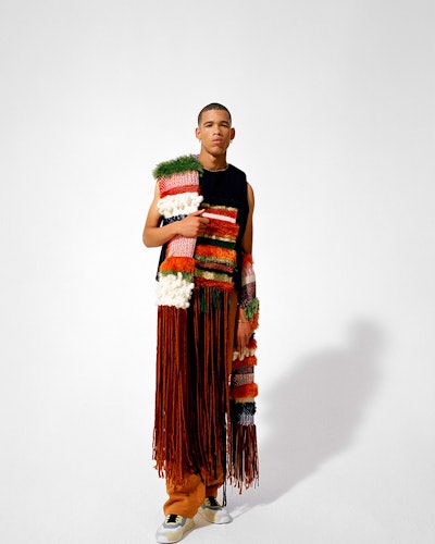 A model wearing a black top with a knit stripe and a long fringe, and a multi-colored knit scarf by ...