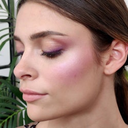 A woman with her eyes shut posing with purple blush applied to her cheeks