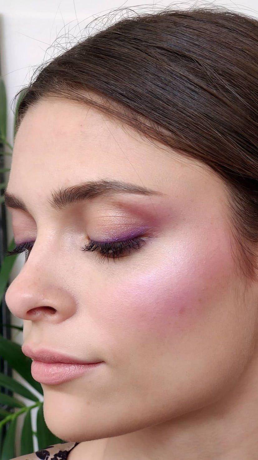 A woman with her eyes shut posing with purple blush applied to her cheeks