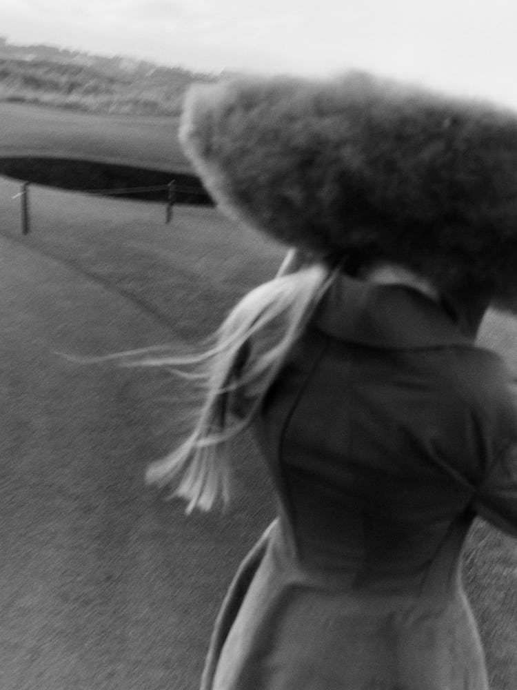 Black and white photo of model in field with furry hat.