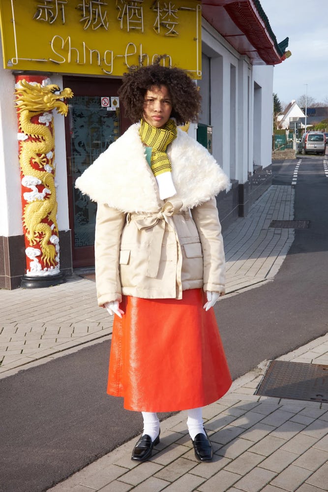 A model wearing  beige jacket, yellow-white scarf, and an orange leather skirt by Meryll Rogge