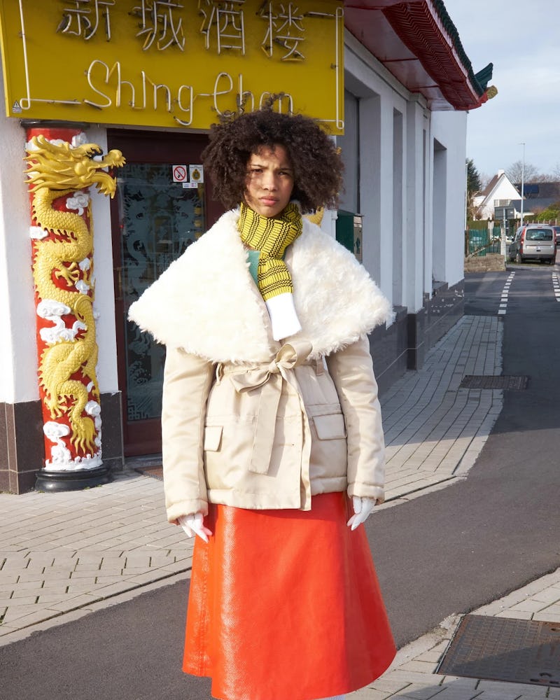 A model wearing  beige jacket, yellow-white scarf, and an orange leather skirt by Meryll Rogge