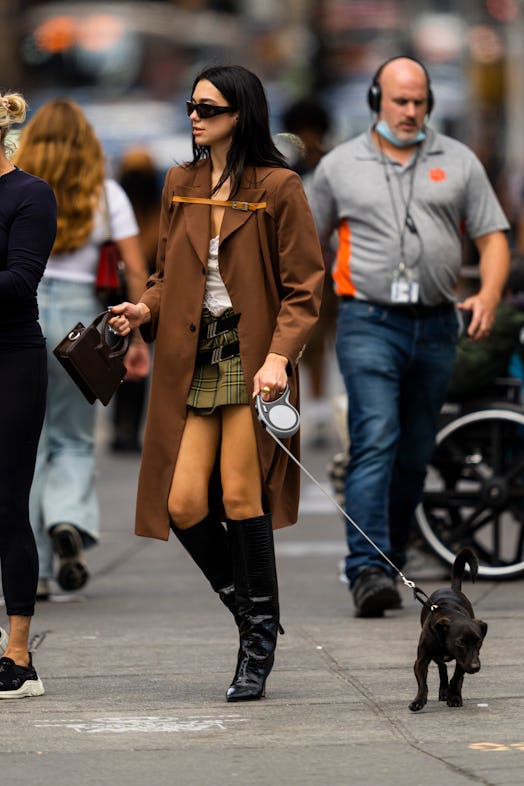 Dua Lipa walking a dog wearing a brown coat, black heels, and carrying a black Luar bag
