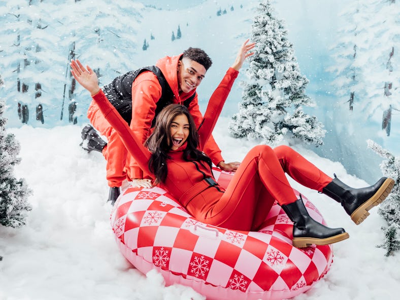 A couple sits in a checkered tube from FUNBOY's winter 2021 collection on a snowy mountain.
