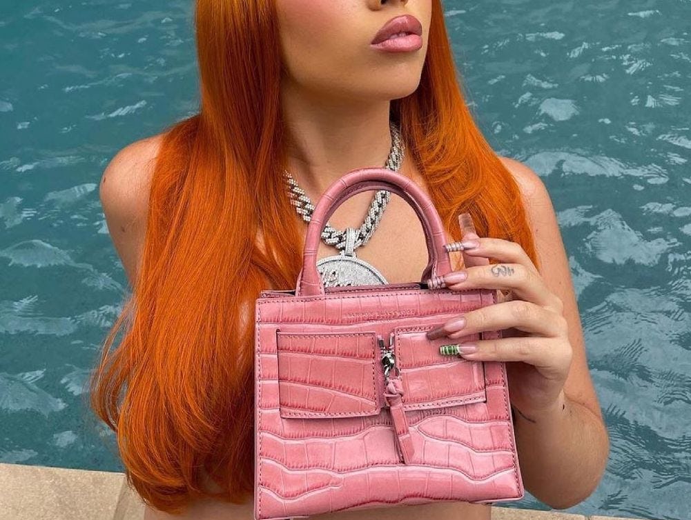 Woman with red hair, wearing a silver necklace, pink purse, and her nails manicured with crocodile n...