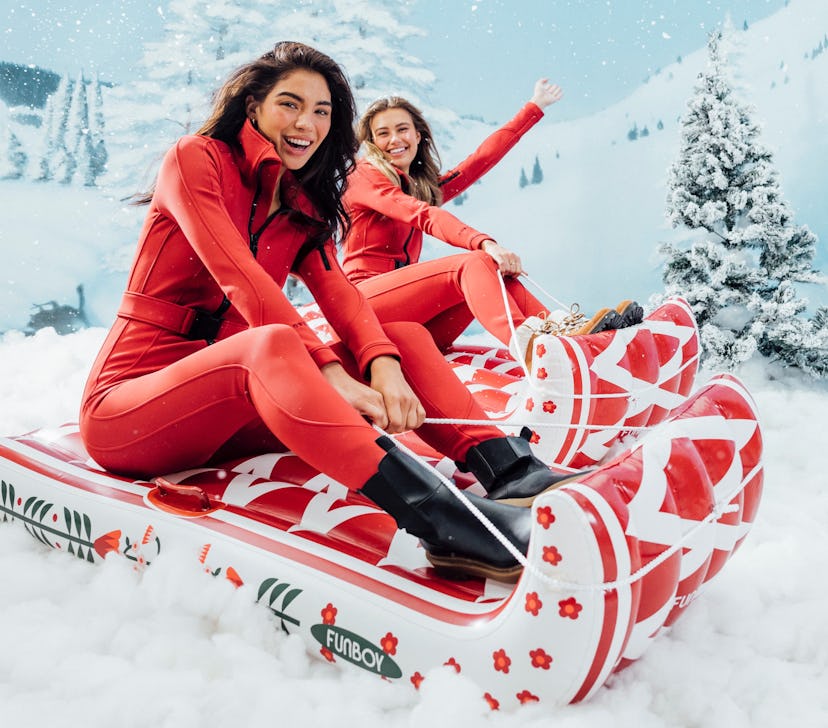 Two women sit in sleighs from FUNBOY's Winter 2021 collection on a snowy mountain.