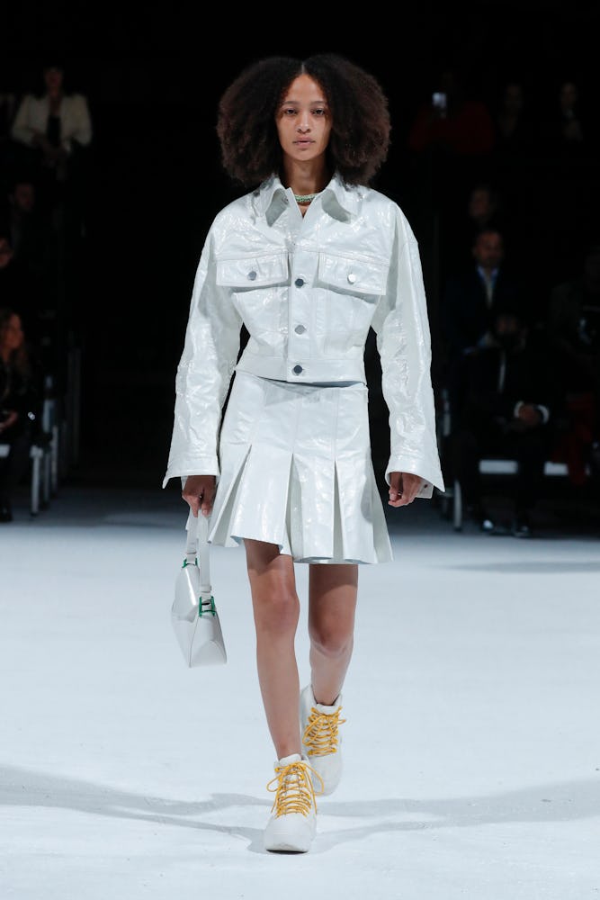 Model walking the runway in Bottega Veneta Spring 2022, in a white jacket and matching mini skirt 