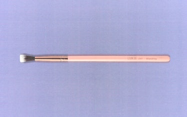 a pink makeup brush against a lavender background