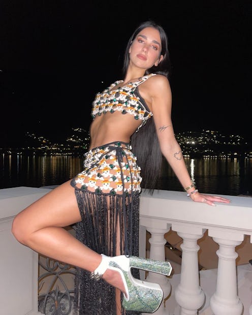 Dua Lipa in skirt and top posing leaning back against balcony