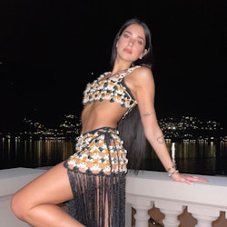 Dua Lipa in skirt and top posing leaning back against balcony