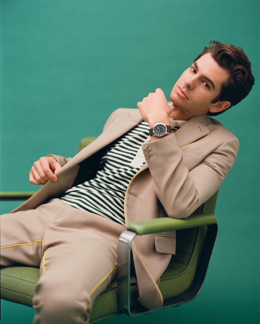 Andrew sitting on a green chair wearing a Fendi suit, a Rhude polo stripy shirt and a Citizen watch