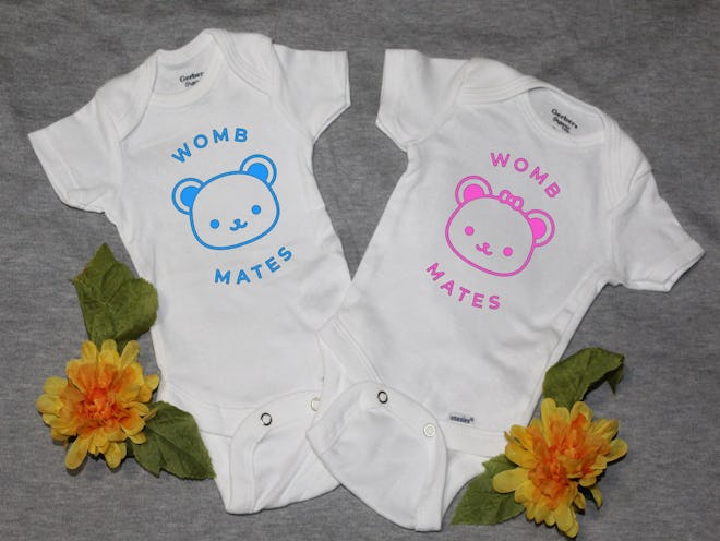 Flat lay of two baby onesies; one pink, one blue, both say "womb mates"