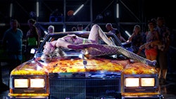 A still from 'Titane', a woman in fishnet stockings reclines on the hood of a car painted in flames.