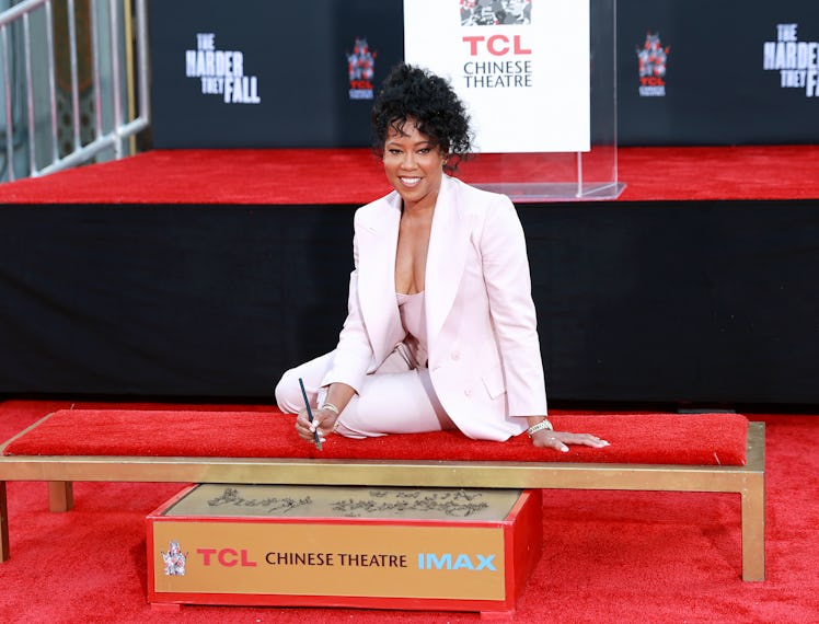 Regina King in a powder pink suit sitting down while getting her handprints immortalized