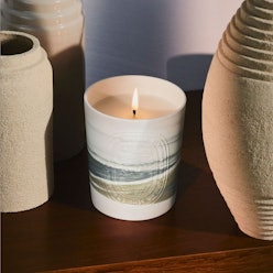 A luxe candle in a cream-beige-navy candleholder next to three vases
