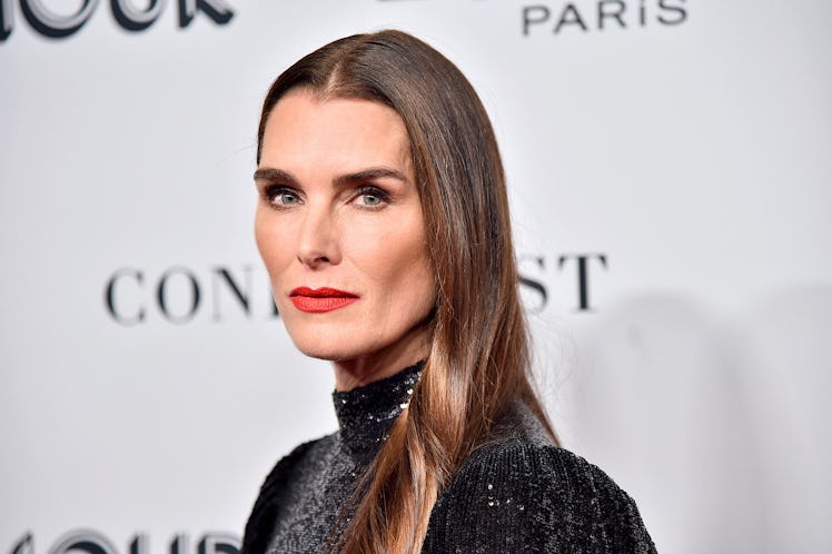 Brooke Shields at a red carpet with straight hair, red lipstick and a shimmery black gown 